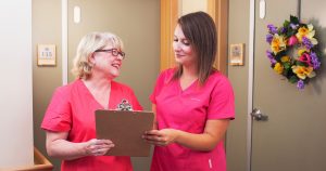 Two nurse next door care givers discussing an elderly couple and how to get them out of the hospital and back into their home