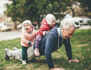 grandfather doing a push up with two grandchildren on his back symbolising the power of happier ageing