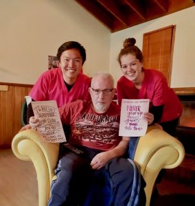 Nurse Next Door client with two caregivers holding signs of affirmation and positivity